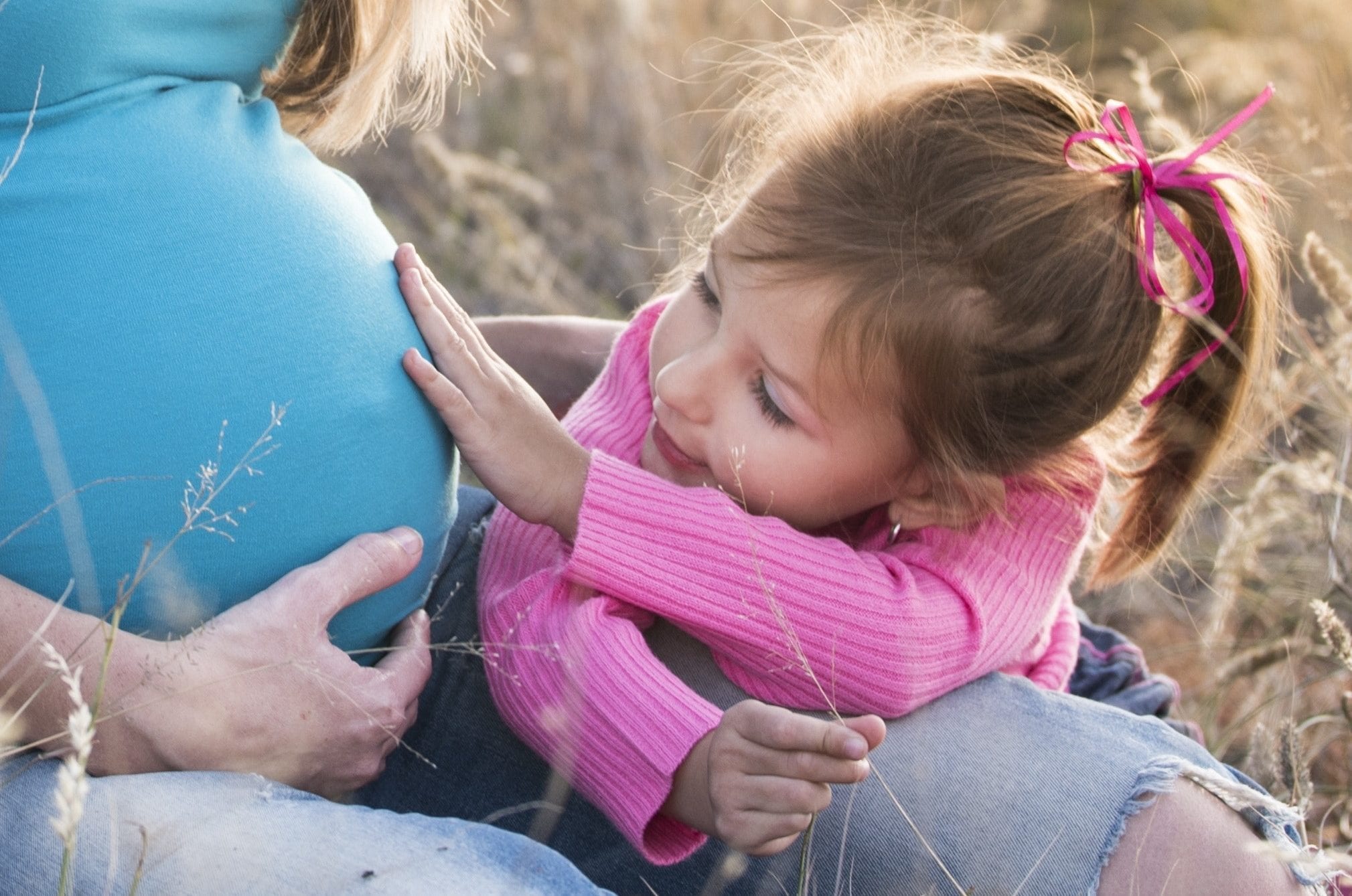 young girl with hand on moms pregnant belly; highlighting fertility over forty