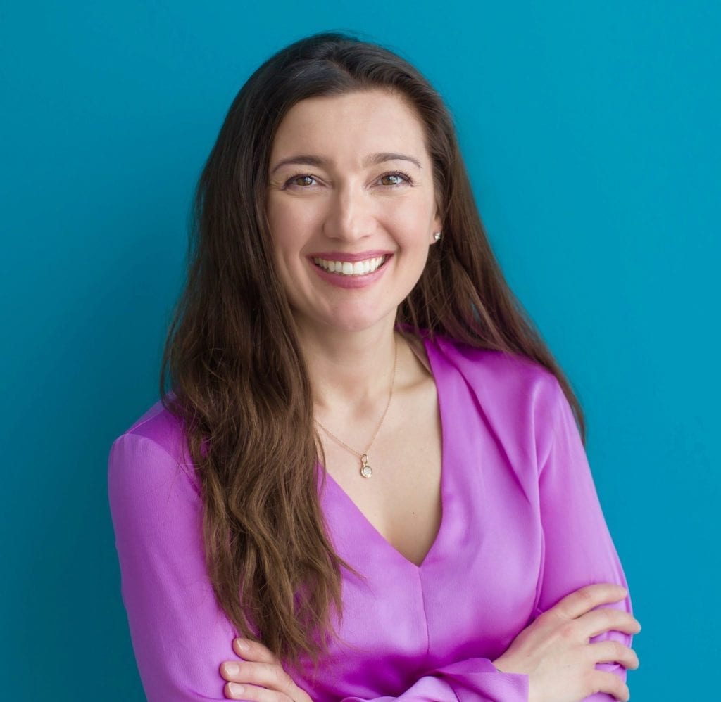 Dr. Emina Jasarevic headshot wearing pink blouse with long dark hair; learn more about our team