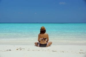 Woman in a bikini sitting on a beach with clear blue water and sky; highlighting managing anxiety