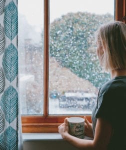 woman staring out of window with snow outside; highlighting seasonal affective disorder in the winter
