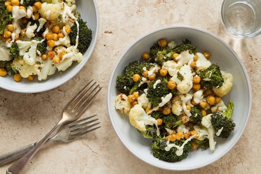 Top view of two roasted buddha bowls with cashew dressing in white bowls on a counter