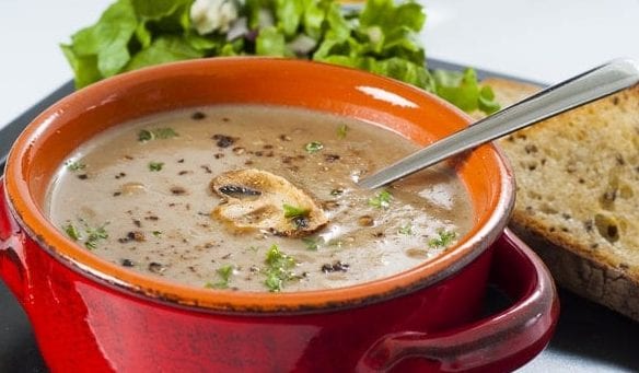 Vegan wild mushroom soup served in a red bowl with gluten free bread on the side