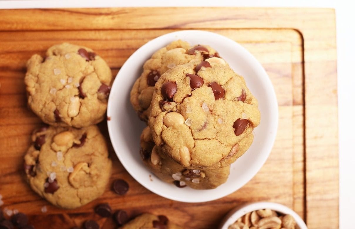 Vegan quinoa chocolate chip cookies on a wooden cutting board with a small white bowl holding a few cookies