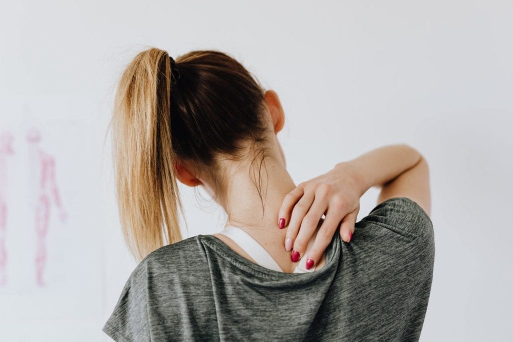 Woman pressing on a trigger point on her back, highlighting massage therapy as a treatment for headache relief.