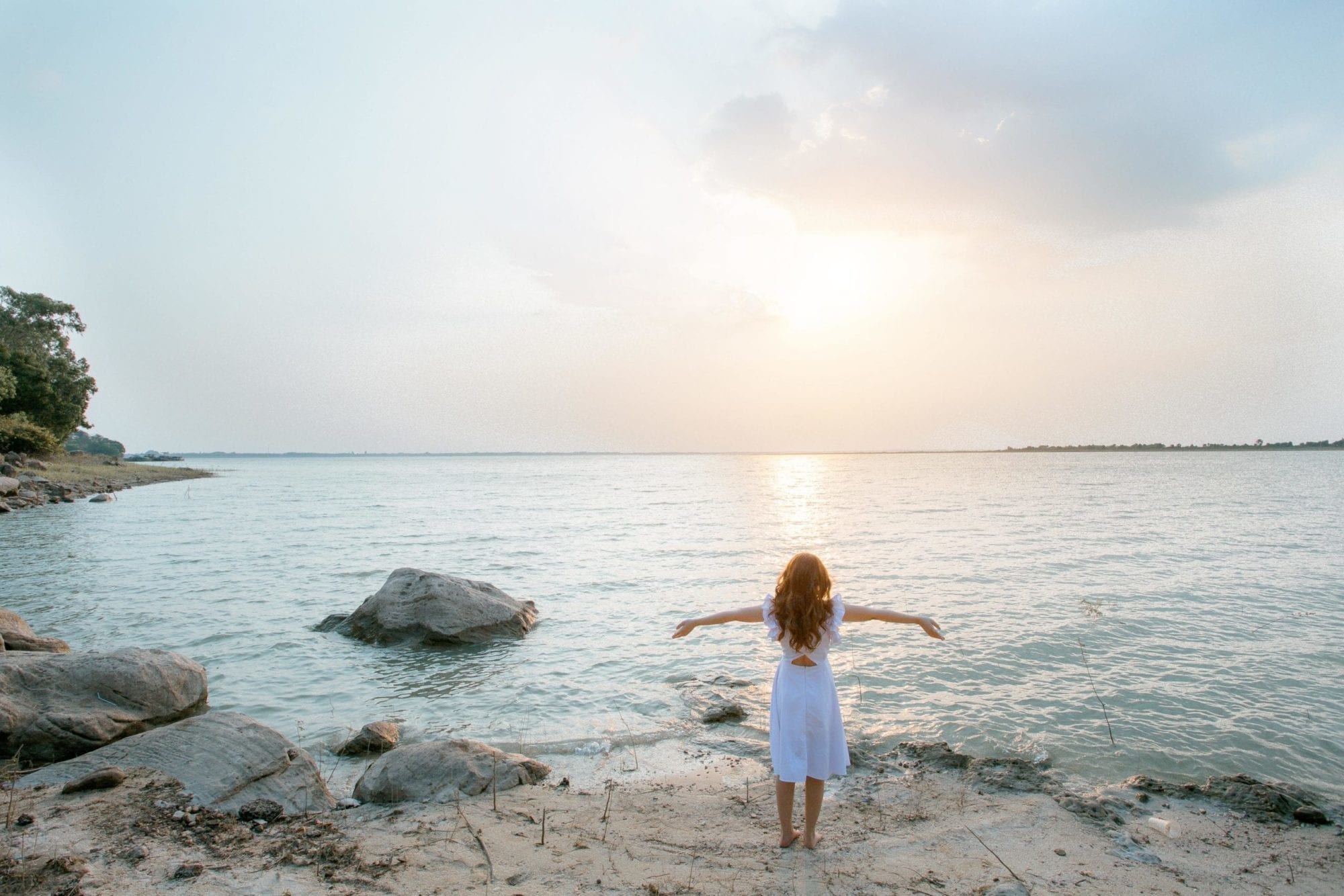 Woman with outstretched arms, facing the sun on the coast, having found chronic pain relief in neural therapy