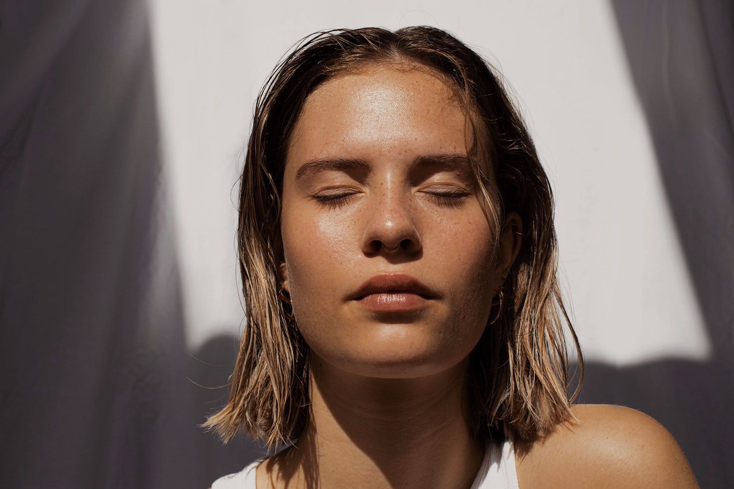 Woman with shoulder length blonde hair and eyes closed sitting in bright light; relating to light therapy for SAD.