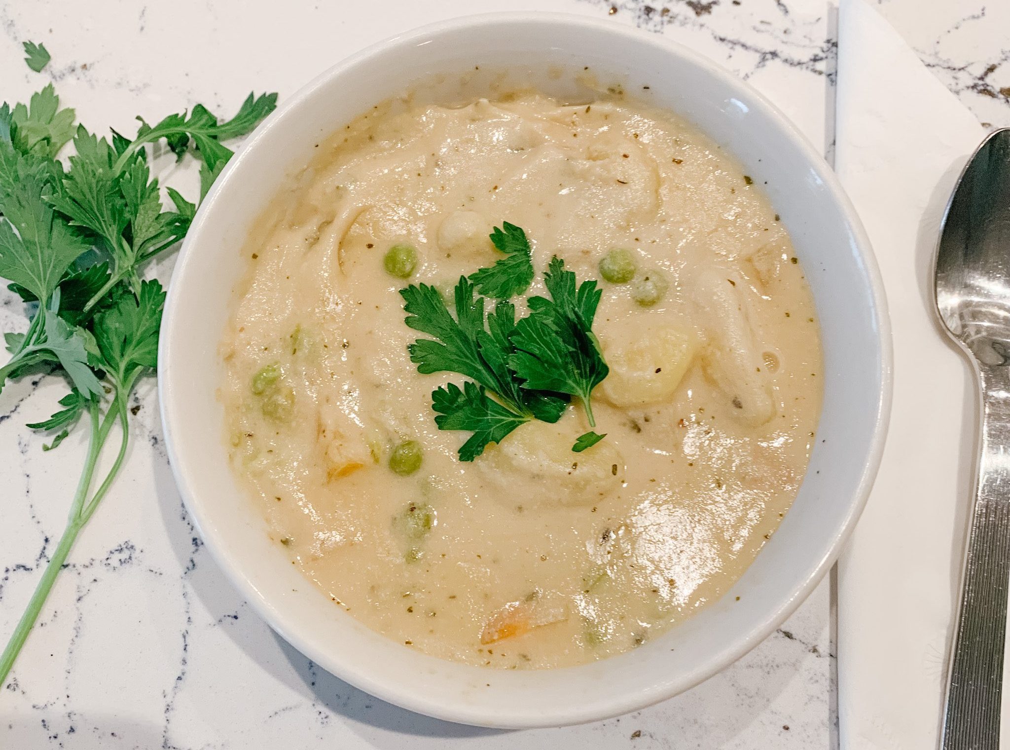 Vegan Italian Gnocchi Soup in a white bowl with leaves of parsley as a garnish.