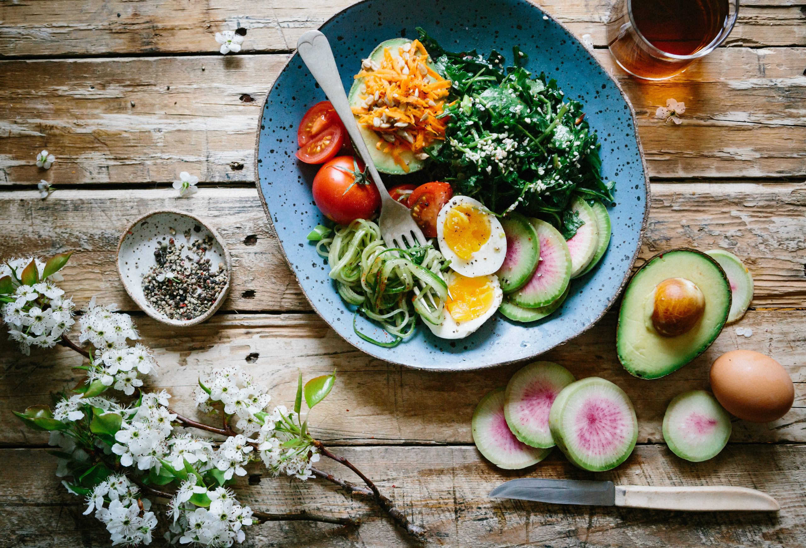 top view of a bowl of nutritious metabolic balancing food including an avocado, spinach, eggs, radish, tomatoes and spiralized zucchini.