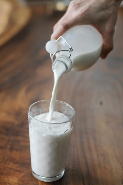 milk being poured into a glass from a glass bottle over a wooden table