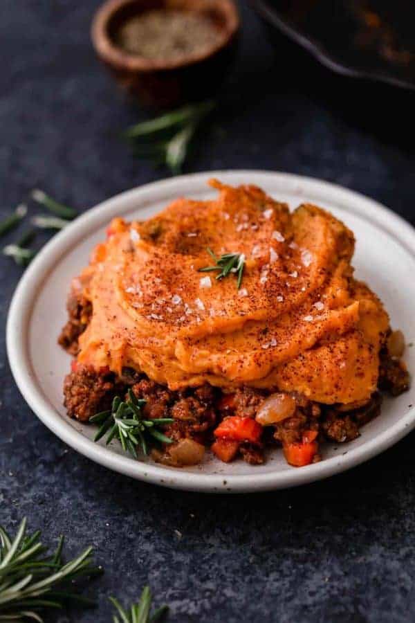 a tabletop view of gluten-free sweet potato shepherd's pie, with herbs around the bowl for decoration