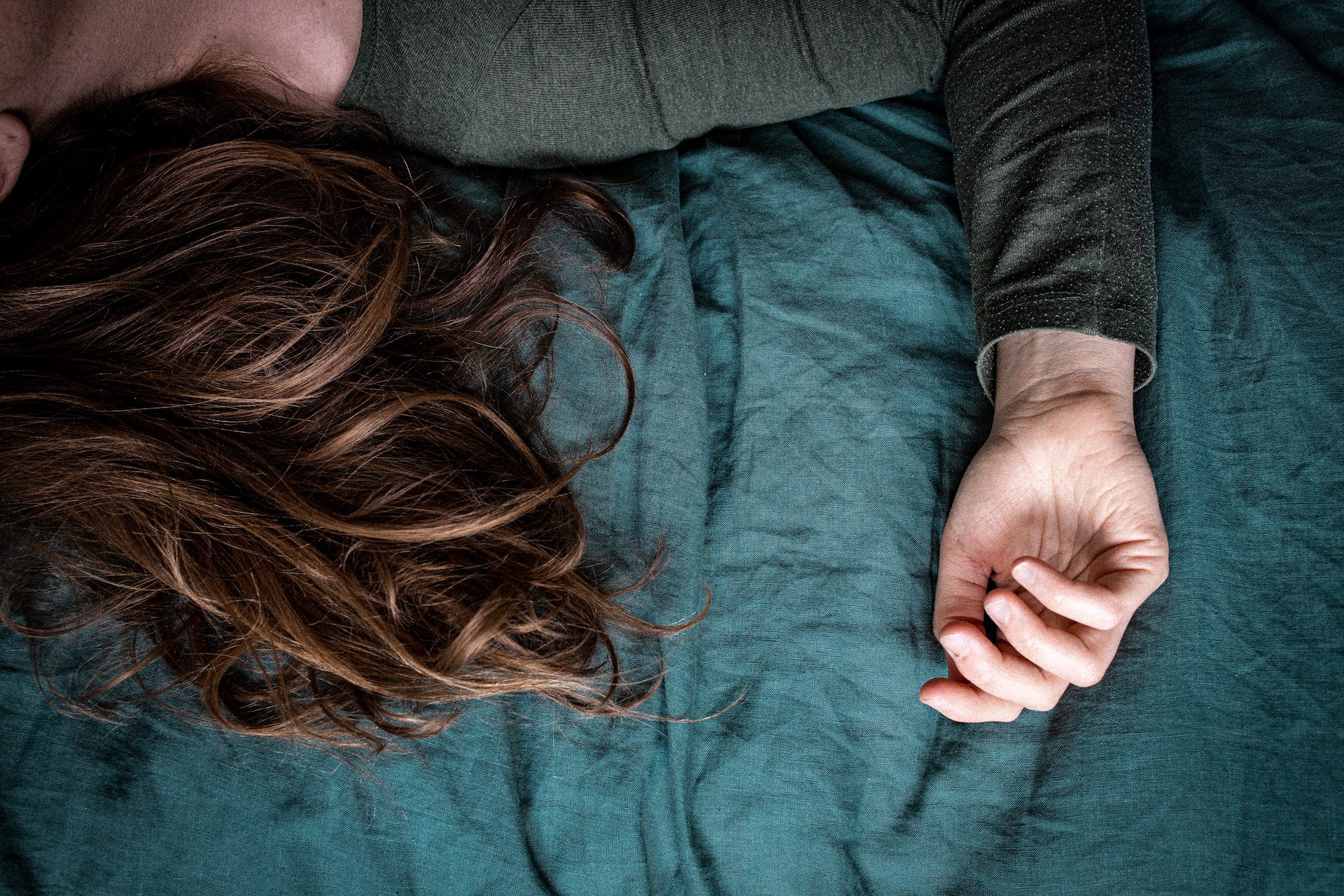 woman lying on bed with teal bedding and a dark green shirt, lethargic before iron iv infusion