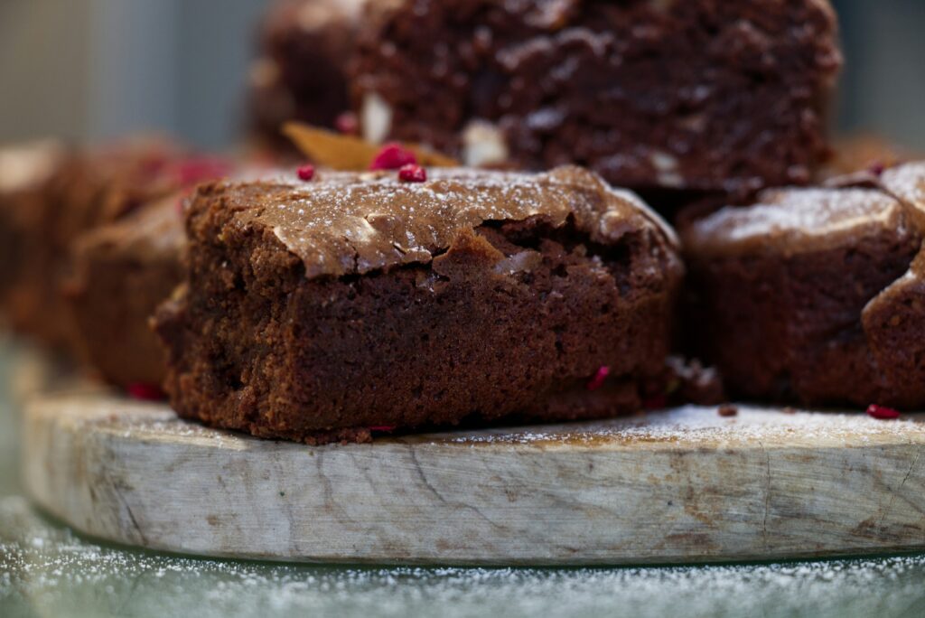 Made from a fudgy brownie recipe, a stack of brownies sit on a wooden cutting board with raspberry bits and icing sugar