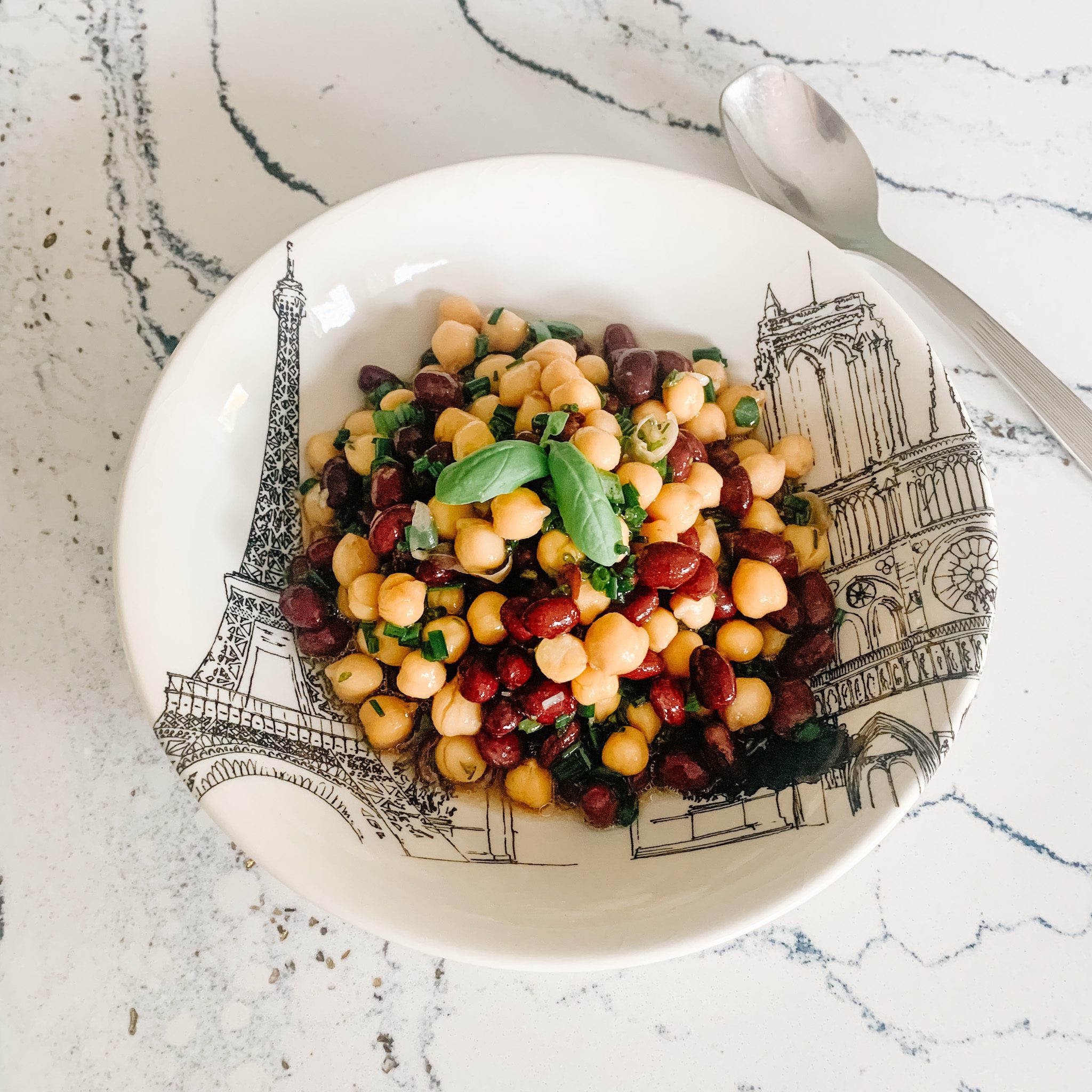 top down view of a bowl of bean salad on a marble countertop with a spoon beside the bowl